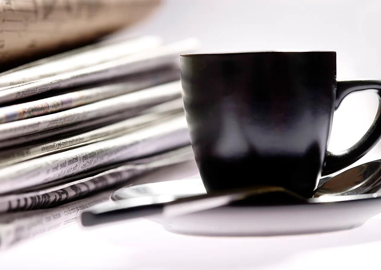 A black coffee cup and a stack of newspapers meant to symbolize catching up on news